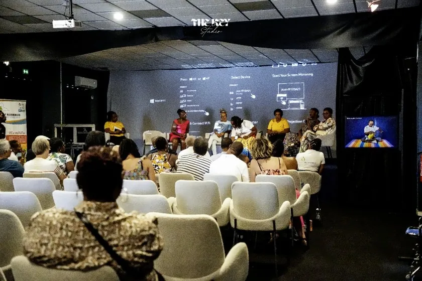 Une salle de projection : le public, vu de dos, écoute les intervenantes assises devant l’écran